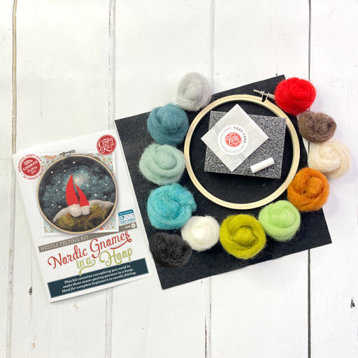 Brightly coloured felt wool, a hoop, needle and instructions for the Nordic Gnome in a Hoop felt kit lay on a white wooden floor 
