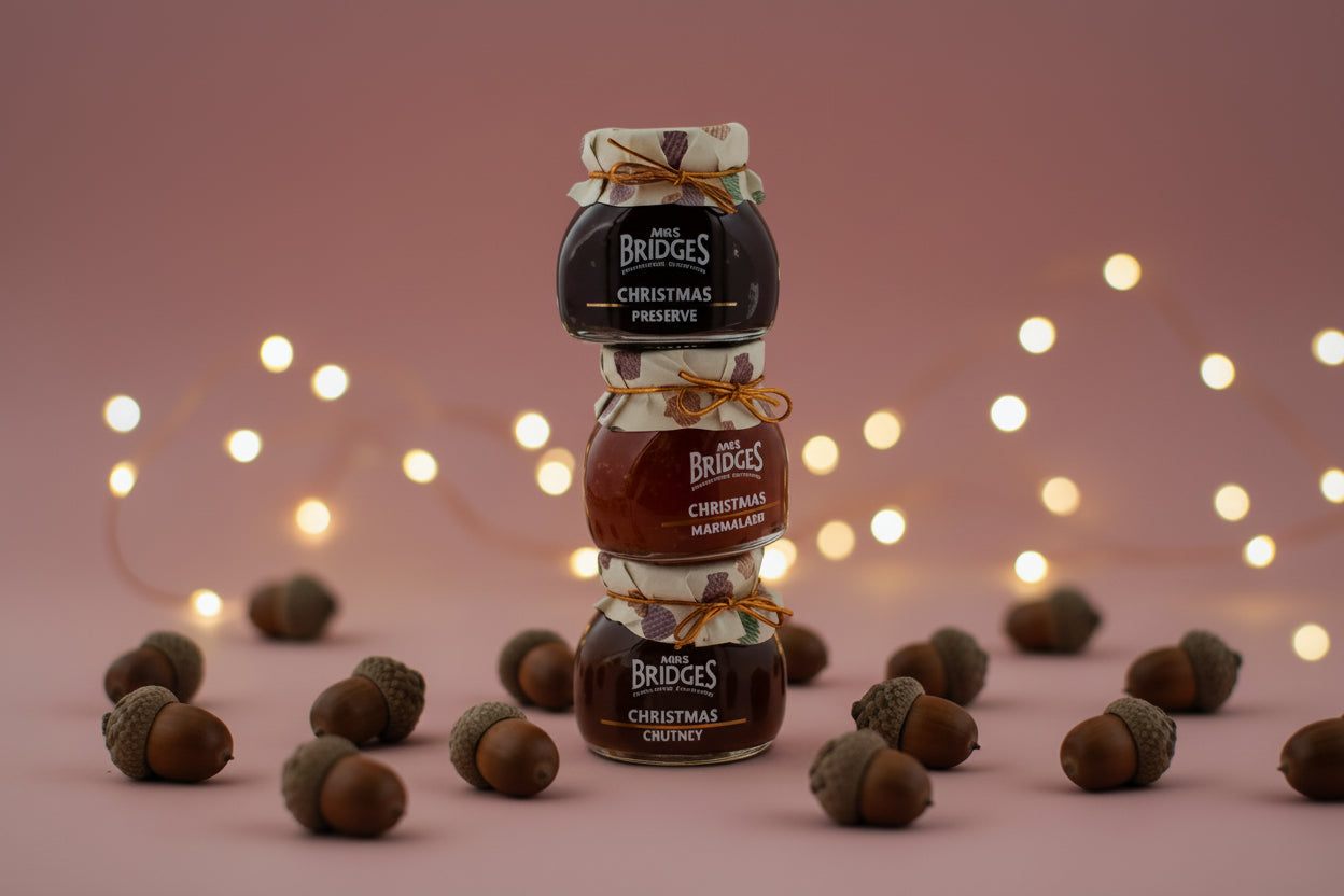 Three stacked glass jars of The Bridges Christmas spread, including Christmas Preserve, Christmas Marmalade, and Christmas Choclate, tied with orange and cream ribbons on a white background. - Image