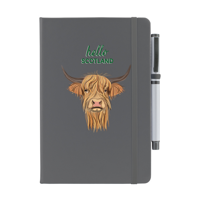 Soft Touch grey notebook featuring a Highland Cow and the test reads 'hello SCOTLAND'. A grey strap closes over the right hand side with a matching pen.