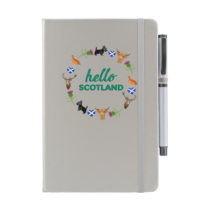 A beautiful designed light grey notebook with the words 'Hello Scotland' in green, featuring elements of Scottish culture and scenery. A light grey strap closes over the right hand side with a matching pen.