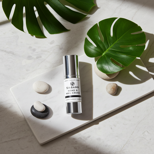 Silver cylinder of Hand & Nail cream on a marble surface with green foliage - Image
