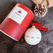 A white bauble with a red ribbon features the word Edinburgh in gold text and a print of the Edinburgh skyline. It sits next to a red presentation box on a grey fur rug. 