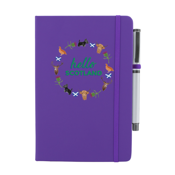 Purple notepad with pen features a circular prints of Scottish Icons including the St Andrews Flag in a loveheart shape, a pheasant and a deer. A matching strap closes on the right hand side.