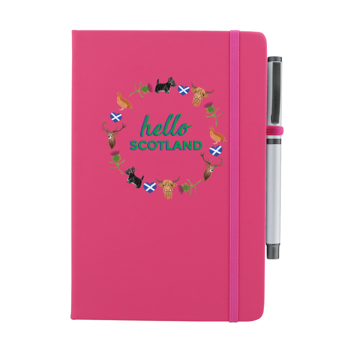 Pink notepad with pen features a circular prints of Scottish Icons including the St Andrews Flag in a loveheart shape, a pheasant and a deer. A matching strap closes on the right hand side.
