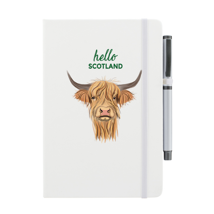 Soft Touch notebook featuring a Highland Cow and the test reads 'hello SCOTLAND'. A white strap closes over the right hand side with a matching pen.