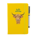 Soft Touch yellow notebook featuring a Highland Cow and the test reads 'hello SCOTLAND'. A yellow strap closes over the right hand side with a matching pen.