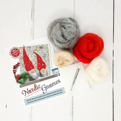 Grey, red and cream balls of felt wool, a needle and instructions for the Nordic Gnomes kit lay on a white wooden floor 
