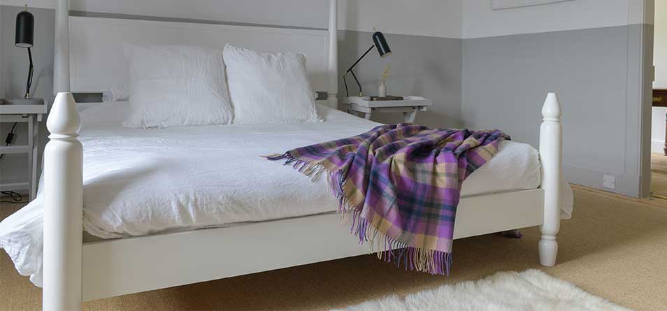 A white bed spread in an openly lit bedroom features the Historic Scotland Coorie Tartan Throw.