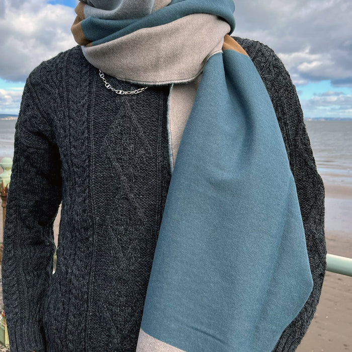 Person wears a grey Aran Jumper with the Block Scarf which is blue, cream and tan. 