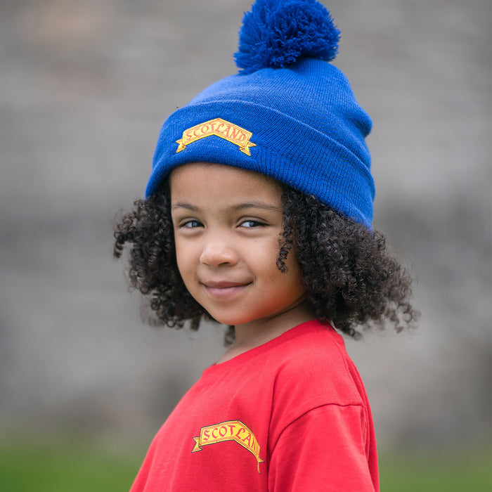 Child wears a blue beanie hat and a red t-shirt. Both have a yellow print that reads 'SCOTLAND'. 