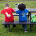 Two children sit at a bench drawing. The view shows the back of the children, one is wearing a red tee with a unicorn motif whilst the other wears a blue one with a knight design. 