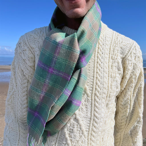 Close up of a person wearing a cream Aran jumper and the Bracken Scarf. Behind is a blue sky and seascape. 