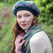 Close up of a person wearing the green and purple Bracken Tartan Tam and wool scarf. 