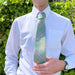 Person stands in front of some greenery wearing a white shirt with the Bracken Tartan Tie. 