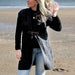 Pearson with blonde hair stands on a beach wearing the charcoal buckle tie cardigan. 