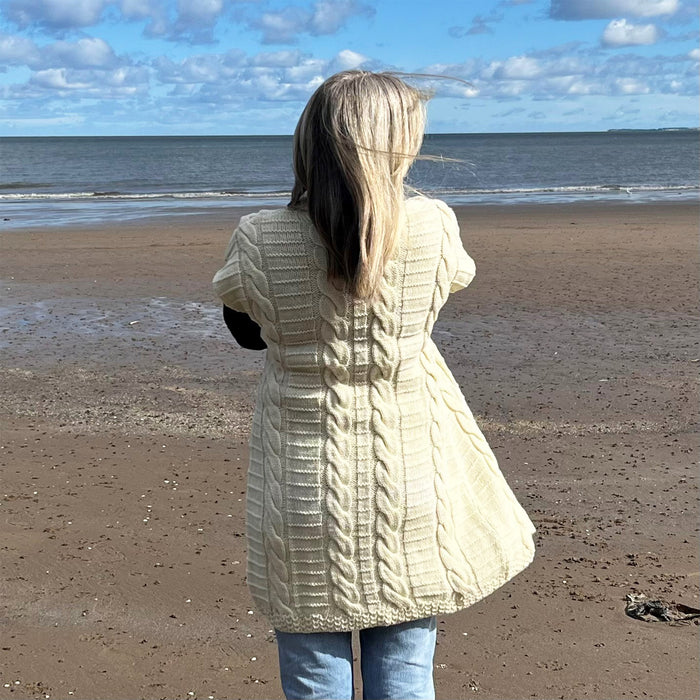 Person standing on a beach facing the sea  wears the buckle cardigan in cream 