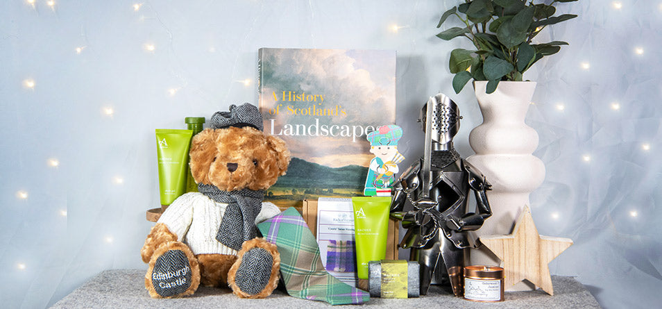 A selection of gifts including a teddy bear, skincare products and homewares and arranged on a table in front of a grey background with fairy lights. 