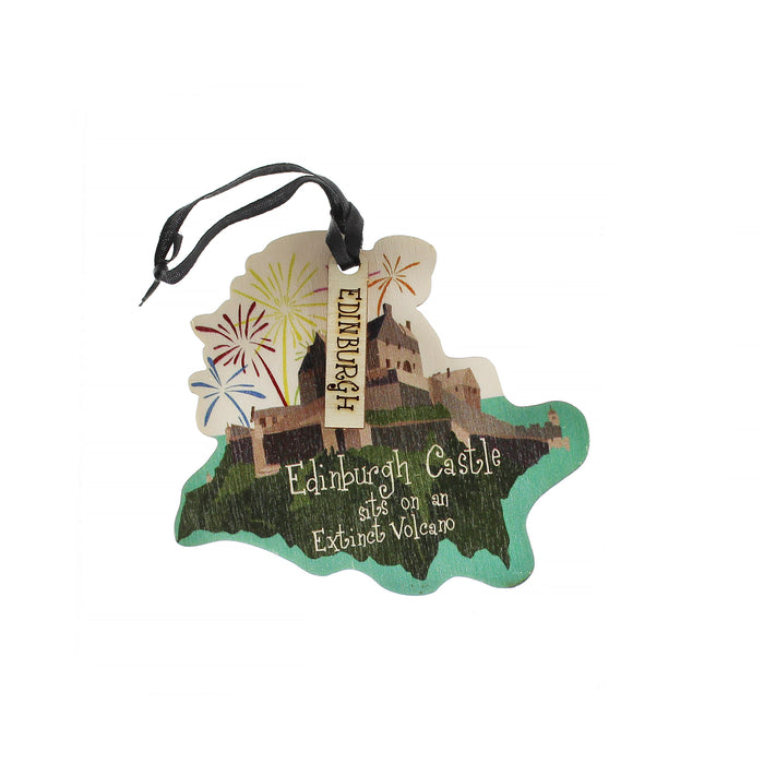 A detailed wooden decoration of Edinburgh Castle sitting on an extinct volcano with fireworks on the background. The decoration also features a small black ribbon and a tag with the text Edinburgh.