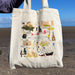 Person holds the Edinburgh Cityscape Tote whilst standing in front of a beach and blue sky. The tote features some of Edinburgh's most loved landmarks. 