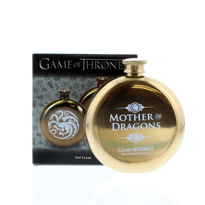 Gold circular tin flask with box behind. The flask is an official Game of Thrones piece with the text 'Mother of Dragons' printed in white.  