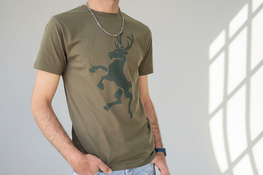 Person wears a army green t-shirt with a dark green stag print. The background is trees lit by the sunshine. - Image