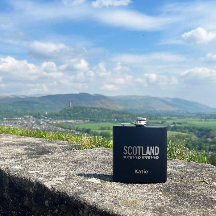 Dark blue flask sits on a wall of Stirling Castle. In the background is a mountain-scape and blue skies. 