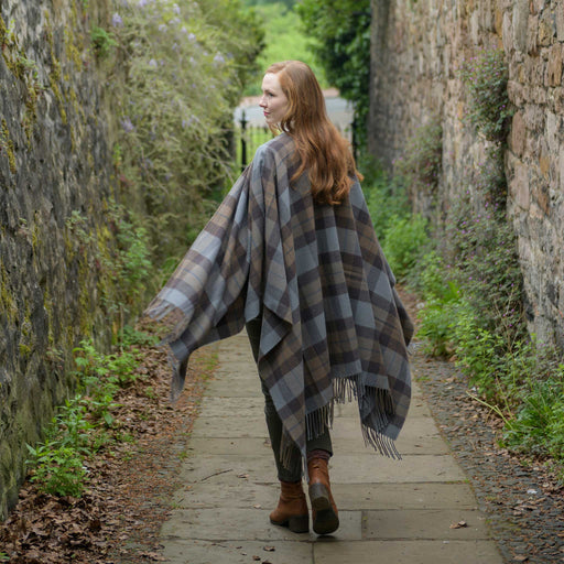 Person stands on a walled path wearing the outlander tartan serape. The tartan features a brown and blue check. 