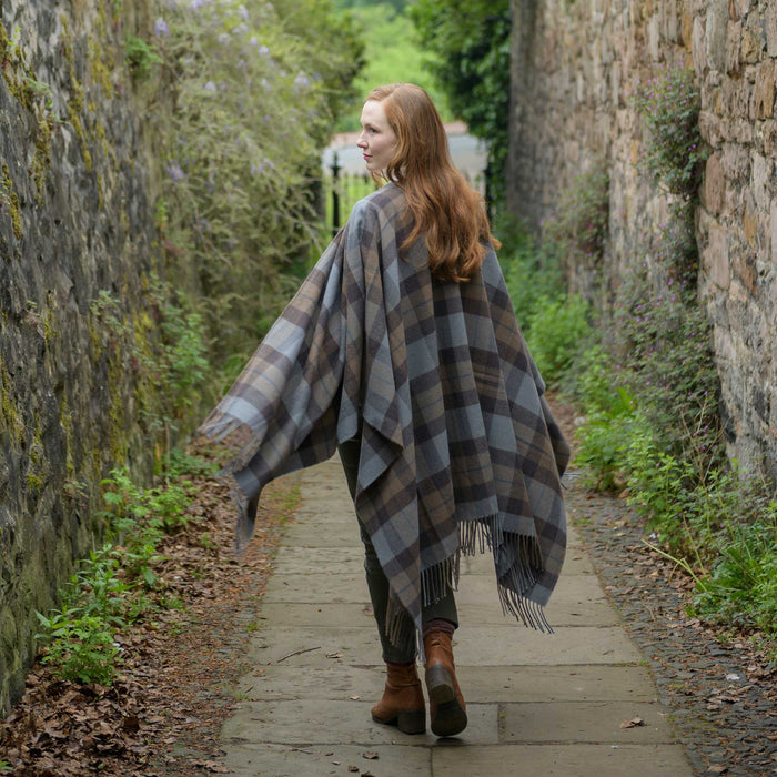 Person stands on a walled path wearing the outlander tartan serape. The tartan features a brown and blue check. 