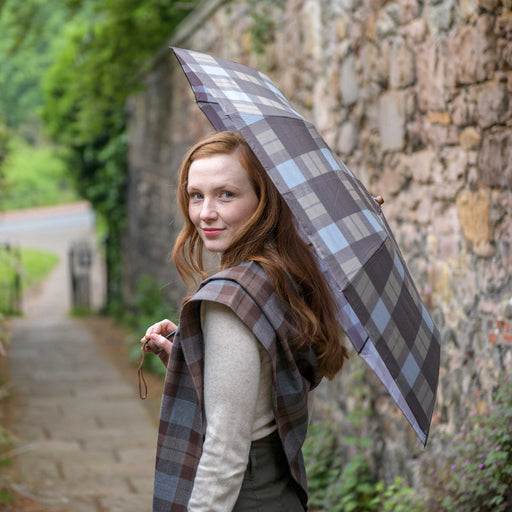 A person on a stone path looks back whilst holding the Outlander Tartan Umbrella. 