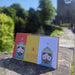 Set of 3 brightly coloured Robert the Bruce greeting cards are displayed on a wall in front of Dunfermline Abbey.