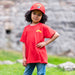 Child wears a red tee and a red cap, both depicting a design of a Scottish knight. 