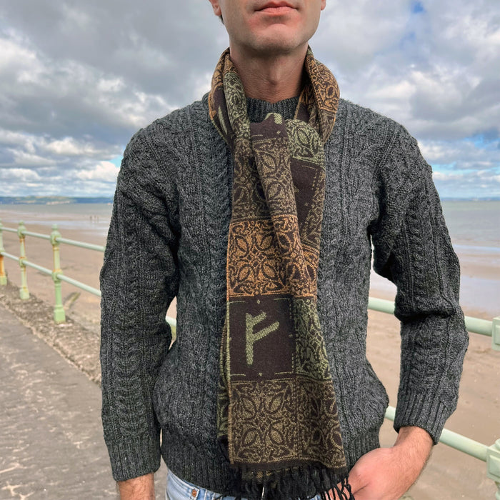 Person wears the brown and green Runes scarf against a sea and beach scene