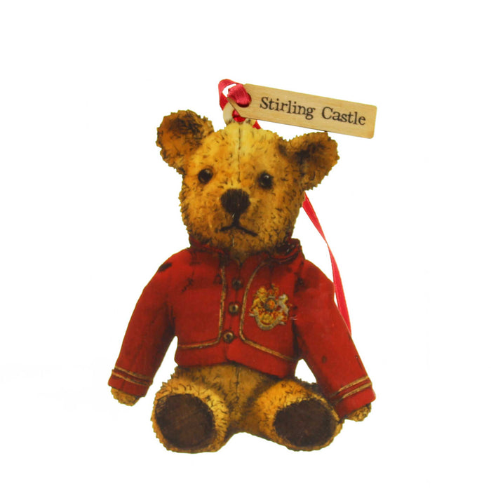 Small wooden tree decoration in the shape of an old fashioned Teddy Bear. The teddy is wearing a red night coat and has a red ribbon for hanging. A small tag on the ribbon reads 'Stirling Castle'. 