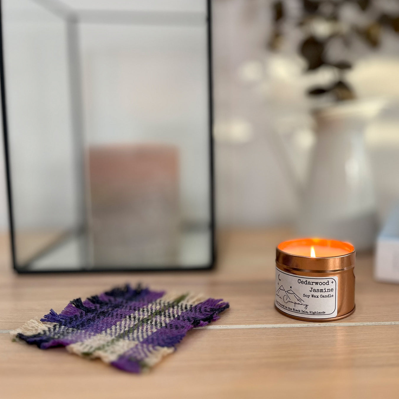 The woven Coorie Coaster is placed next to a warm candle and dried flowers. 