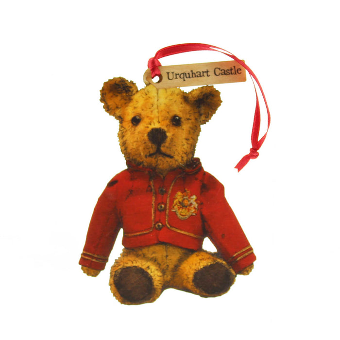 Small wooden tree decoration in the shape of an old fashioned Teddy Bear. The teddy is wearing a red night coat and has a red ribbon for hanging. A small tag on the ribbon reads 'Urquhart Castle'. 