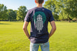 person stands facing away wearing a navy t-shirt. The bacl of the t-shirt show a large print of a viking and a celtic design in green and white.  - Image