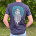 person stands facing away wearing a navy t-shirt. The bacl of the t-shirt show a large print of a viking and a celtic design in green and white. 