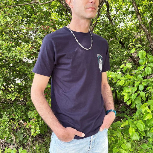 Person stands in front of some green trees wearing a navy t-shirt with a Viking print on the left chest. 