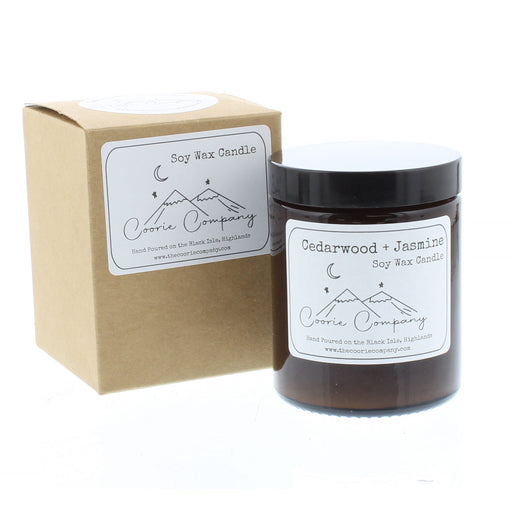 Cedarwood and Jasmine scented candle in a brown jar with a label that shows a simple etching of a mountain top and a crescent moon. Next to the candle is it's brown card box with the same mountain image on a white sticker. 