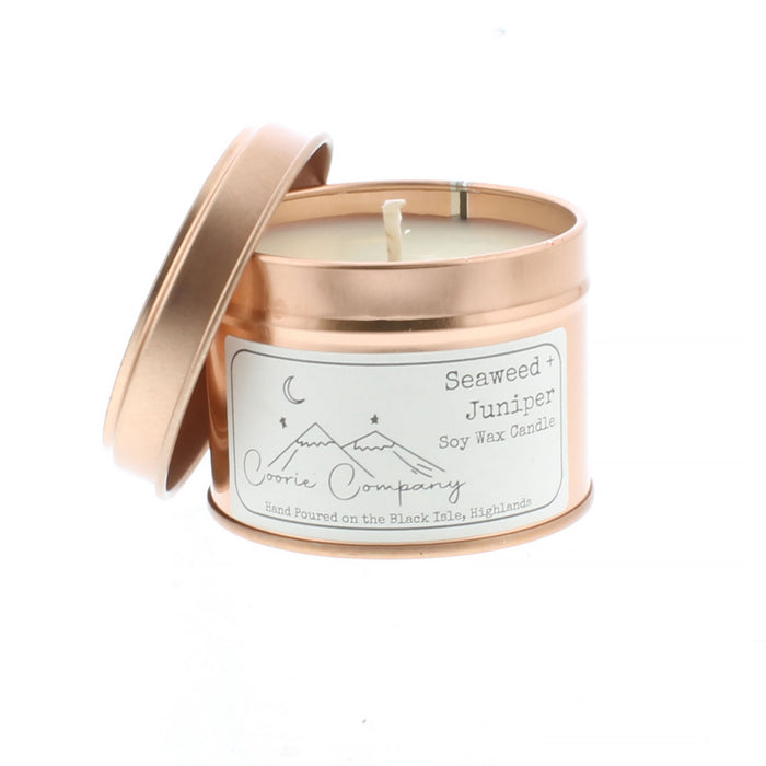 Rose gold tin contains a Seaweed and Juniper scented candle. On the front of the tin is a white label that features a simple etching of a mountain scape and a crescent moon.
