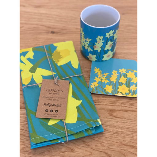 Daffodil printed teatowel, coaster and mug placed on a wooden kitchen work top
