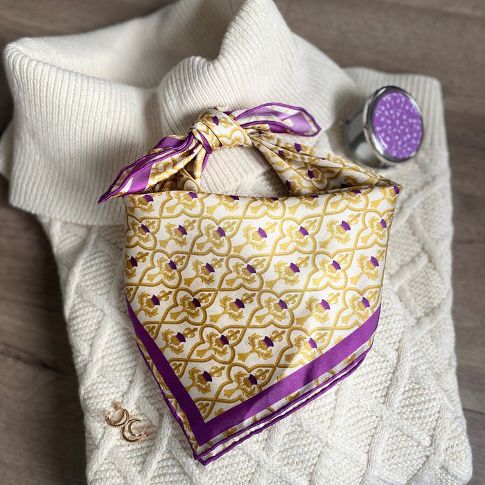 Thistle Print scarf with gold and purple colouring tied on top of a cream jumper, gold earrings and the thistle print compact mirror 