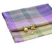 Selection of charms placed on a purple and green tartan 'Coorie' scarf include an orb, swan and small thistle. 
