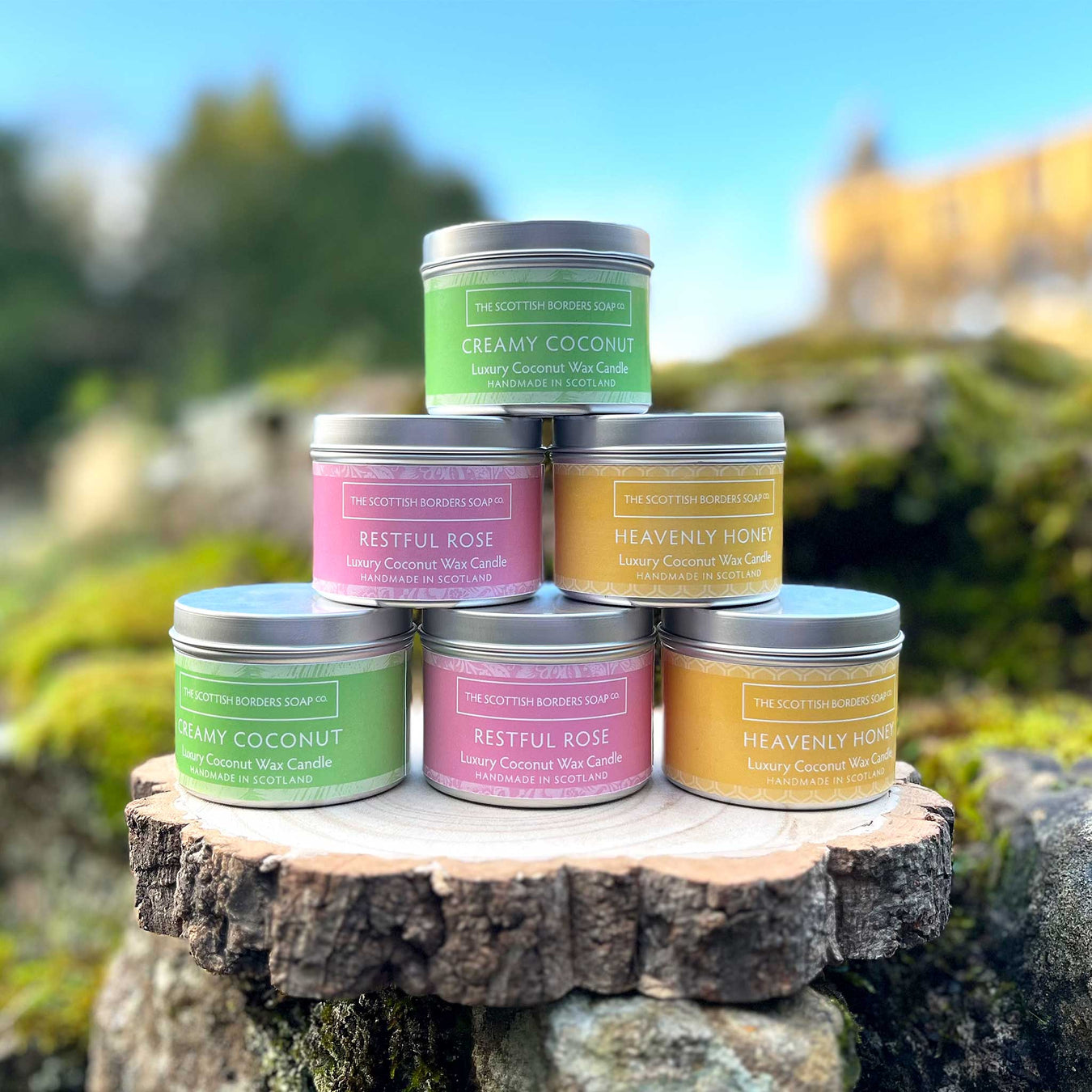 Brightly coloured candle tins sit on some stones and moss in front of a Castle.