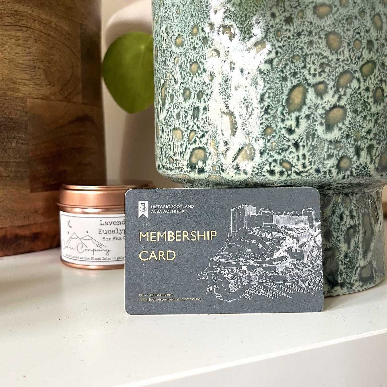 The official Historic Scotland Membership cards sits on a table between some plant pots and next to a bronze coloured candle tin