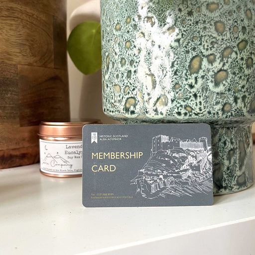 The official Historic Scotland Membership cards sits on a table between some plant pots and next to a bronze coloured candle tin