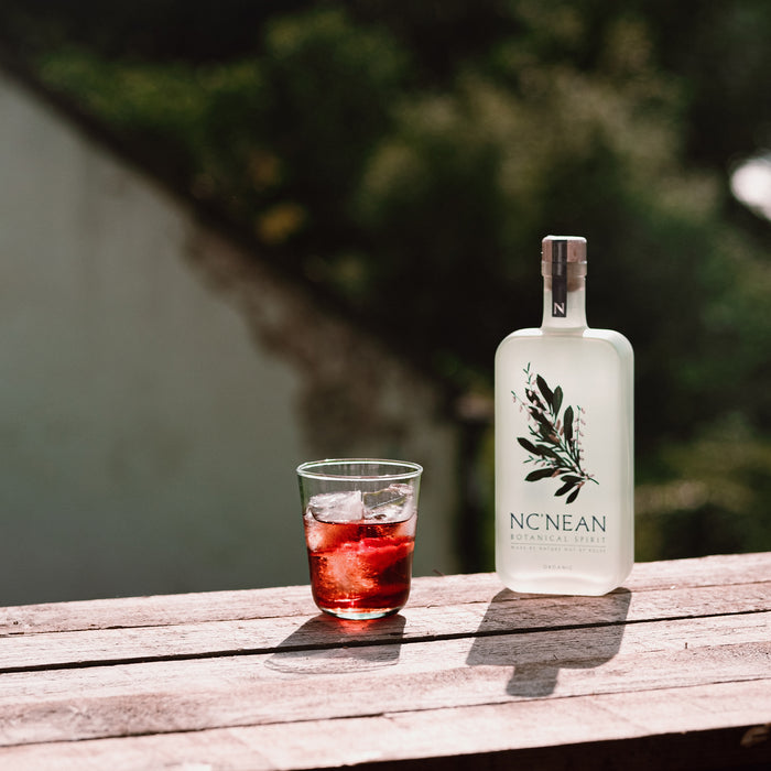 Bottle of NcNean Botanical Spirit next to a glass containing Negroni cocktail