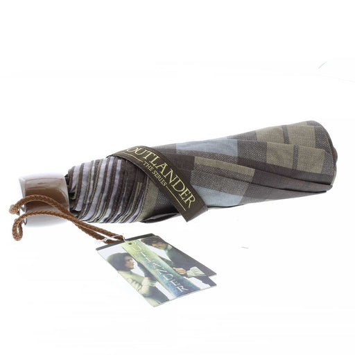 The Official Outlander Tartan on an umbrella features shaded of brown and light blue. The Umbrella is wrapped closed and the closure wrap has the Outlander official text logo embroidered in gold. 