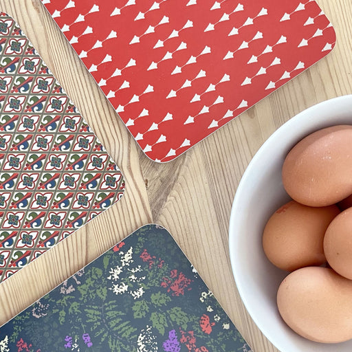 The Stirling Castle Bespoke Pot Holders in a red Tulip, Fleur de Lys and Tapestry print are placed next to a bowl of eggs. 