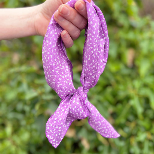 silk scarf showing hanging from hand with a loose knot to base in front of green bushes in soft focus